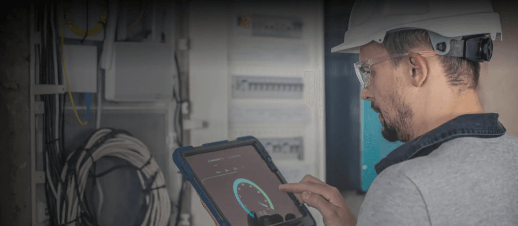 Technician working on a switchboard using a tablet with IoT predictive maintenance system